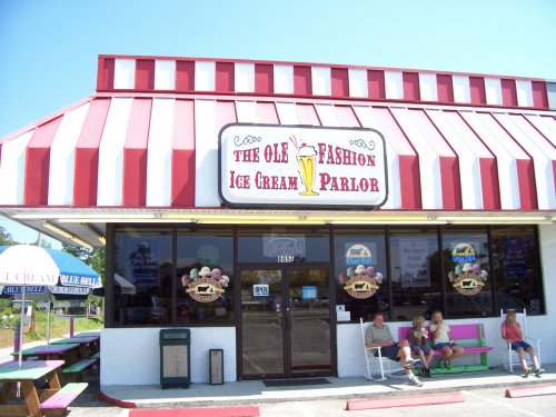 A colorful ice cream parlor with a red and white striped roof, featuring outdoor seating and a welcoming sign.