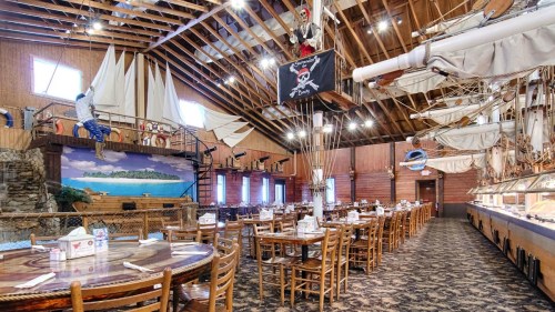 Interior of a themed restaurant with pirate decor, wooden tables, and a mural of a tropical scene.