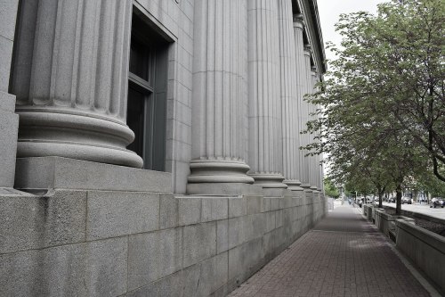 Close-up of a stone building's columned facade, with a tree and sidewalk visible in the foreground.