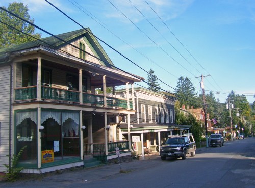 A quaint street scene featuring historic buildings, a restaurant, and parked vehicles under a clear blue sky.