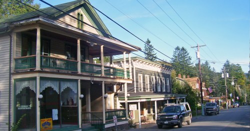 A quaint street scene featuring historic buildings, a restaurant, and parked vehicles under a clear blue sky.