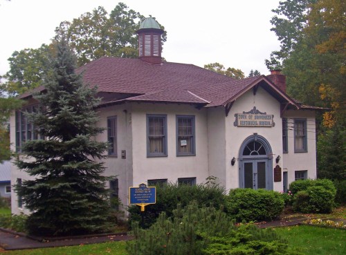 Historic building with a peaked roof, surrounded by trees and a sign reading "Town of Saranac Historical Museum."