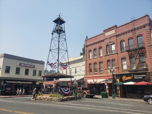 Historic downtown scene featuring a tall tower, brick buildings, and festive decorations on a sunny day.