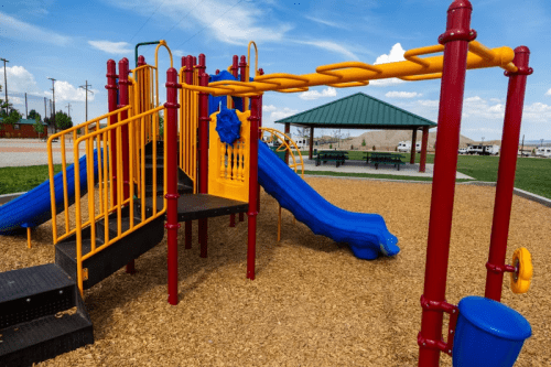 Colorful playground equipment with slides and climbing structures, set on a sandy area under a blue sky.