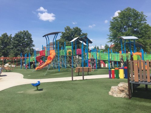 Colorful playground with slides, climbing structures, and benches, set on green grass under a blue sky.