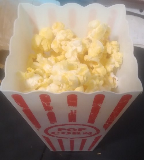 A striped popcorn box filled with fluffy, yellow popcorn.