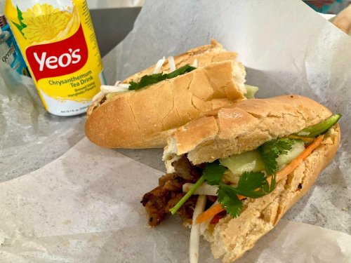 A close-up of two Vietnamese banh mi sandwiches with fresh vegetables, cilantro, and a can of chrysanthemum tea.
