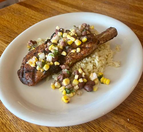 Grilled pork chop on a bed of rice, topped with corn, black beans, and diced vegetables.
