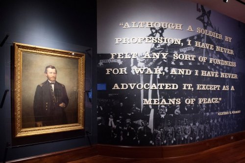 A framed portrait of a soldier beside a wall with a quote about war and peace by Ulysses S. Grant.