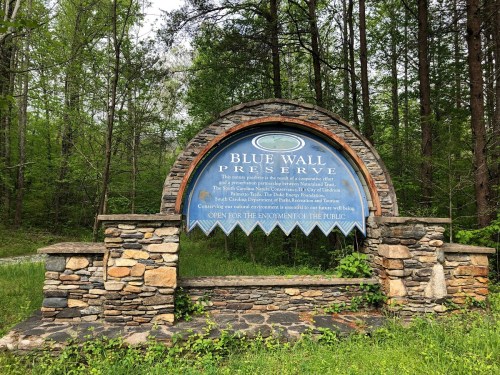 Sign for Blue Wall Preserve, surrounded by trees, detailing the area's natural significance and public access.