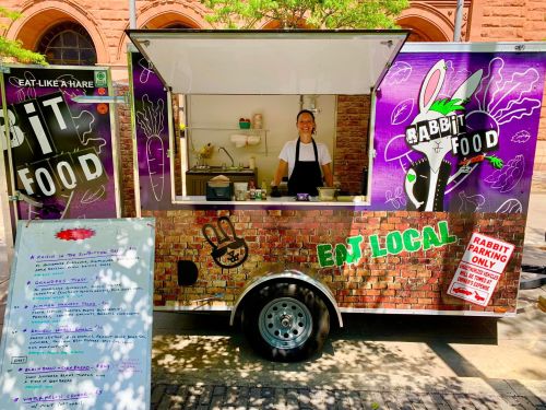 A food truck with a colorful design, featuring a smiling vendor and a menu of local dishes.
