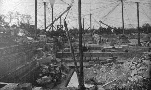 Historic construction site with cranes, stone blocks, and workers amidst a landscape of debris and machinery.