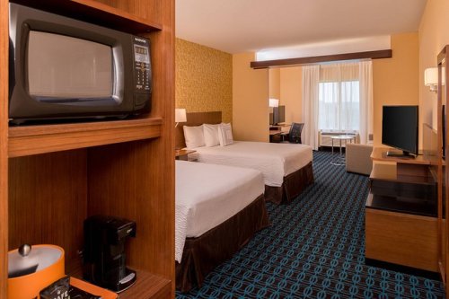A hotel room featuring two beds, a microwave, coffee maker, desk, and a large window with natural light.