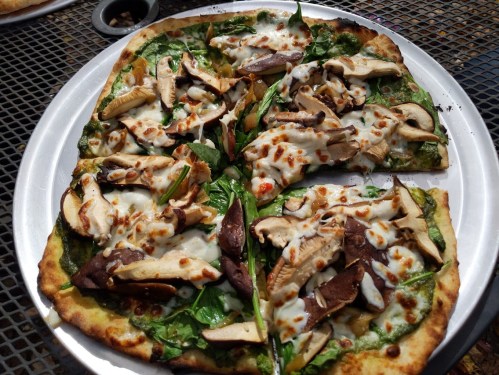 A freshly baked pizza topped with spinach, mushrooms, and melted cheese on a thin crust, served on a metal plate.