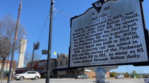 Historical marker for Belton, SC, detailing its incorporation and railway history, with buildings in the background.