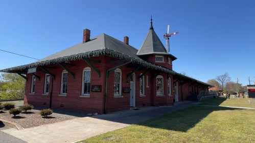 Historic brick train station with a pointed roof and decorative trim, set against a clear blue sky.