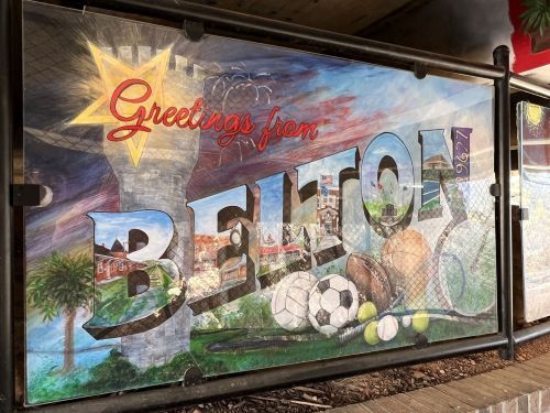 Colorful mural reading "Greetings from Belton" with sports equipment and local landmarks in the background.