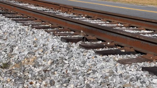 Close-up of rusty railroad tracks beside gravel, with a yellow line visible in the background.