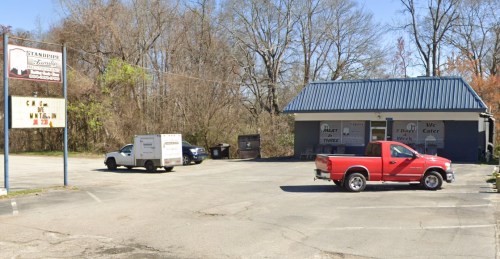 A red pickup truck parked in front of a small catering business with a blue roof and a sign. Trees in the background.