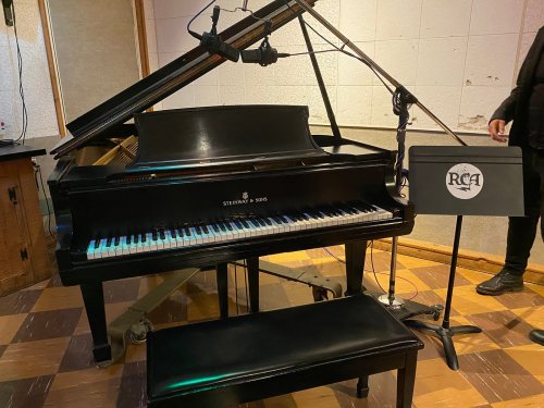 A black grand piano with a microphone set up, next to a music stand displaying the RCA logo.