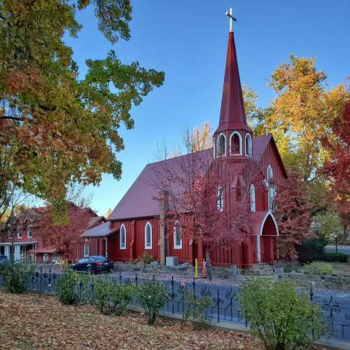 A red church with a tall steeple surrounded by autumn trees and a clear blue sky.