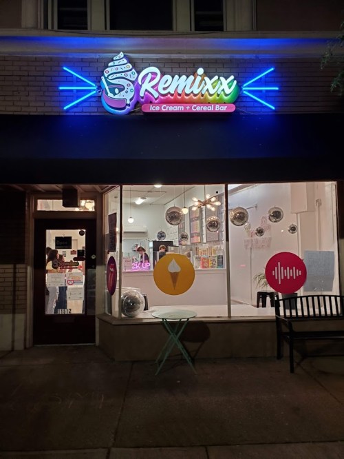 Brightly lit storefront of "Remixx Ice Cream + Cereal Bar" with colorful signage and a bench outside.