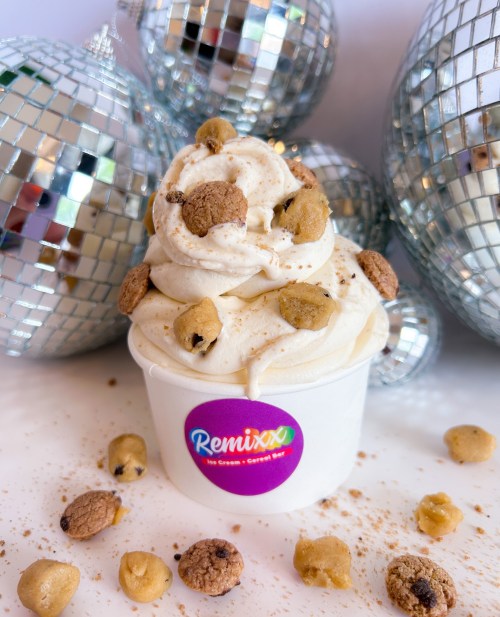 A cup of creamy ice cream topped with cookie dough pieces, surrounded by shiny disco balls.