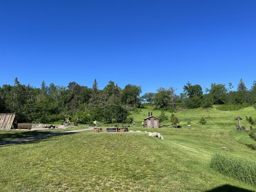 A sunny landscape with green grass, trees, and a small building, featuring people engaged in outdoor activities.