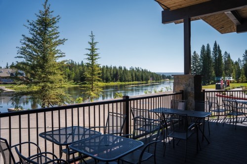 A scenic view from a deck overlooking a calm river surrounded by trees and a clear blue sky. Tables are set up on the deck.