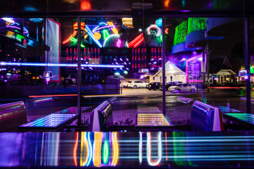 A vibrant neon-lit restaurant interior reflecting colorful lights and street views through large windows at night.