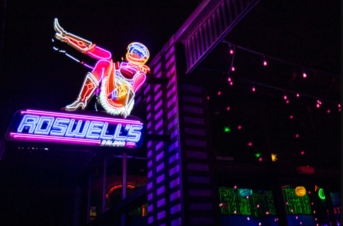 Neon sign for Roswell's Bar, featuring a colorful, retro-style figure and vibrant lights against a dark background.
