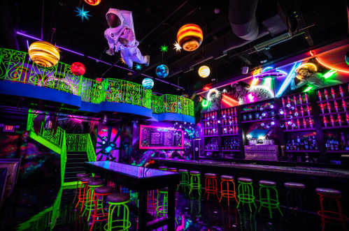 A vibrant bar scene with neon lights, colorful decorations, and a lively atmosphere, featuring a unique design and seating.