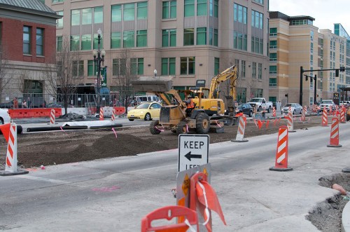 Construction site with heavy machinery, road barriers, and a "Keep Left" sign in an urban area.