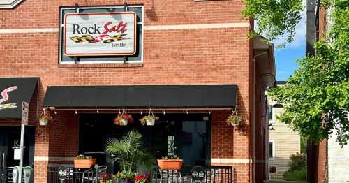 Exterior of Rock Salt Grille, a brick building with a sign, outdoor seating, and hanging flower baskets.