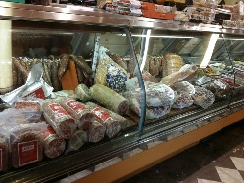 A display case filled with various cured meats, cheeses, and packaged goods in a deli.