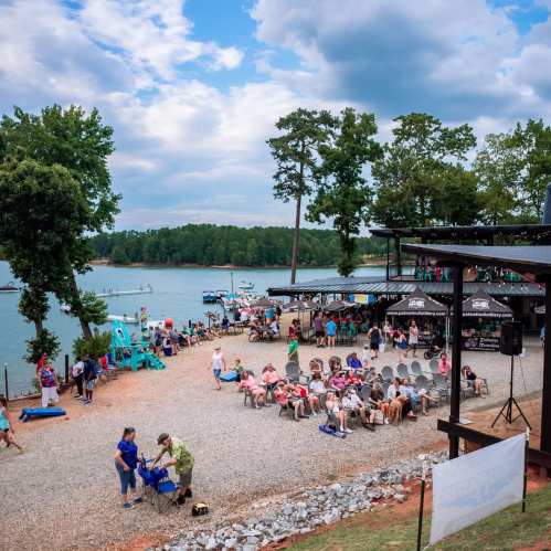 A lakeside gathering with people sitting in chairs, enjoying the view, and activities on the water in the background.