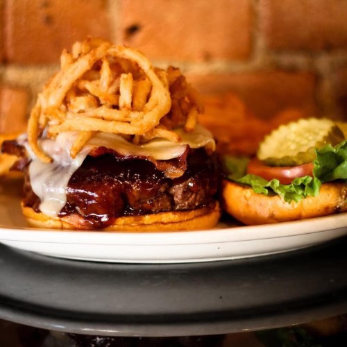 A close-up of a gourmet burger topped with crispy onions, cheese, and barbecue sauce, served on a plate.