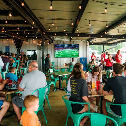 A lively indoor dining area with people enjoying food and drinks, watching a football game on a large screen.