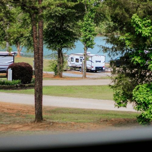 A serene campsite with trailers near a lake, surrounded by trees and grassy areas.