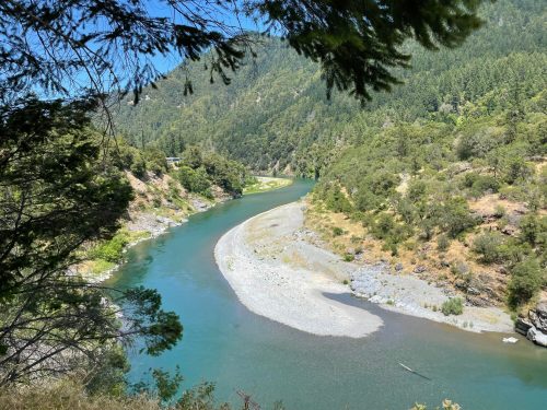 A winding river flows through a lush green landscape, surrounded by hills and trees under a clear blue sky.