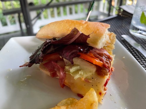 A close-up of a sandwich with layers of meat, lettuce, and roasted peppers on a plate, with a toothpick holding it together.