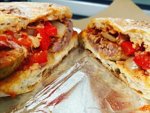 Close-up of a sandwich filled with meat, peppers, onions, and sauce, served on toasted bread.
