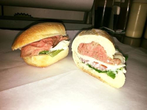 Two sandwiches on parchment paper: one with roast beef and mayo, the other with a pink filling and fresh vegetables.