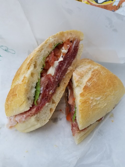 A sandwich with layers of meat, lettuce, and tomato, served in a crusty bread roll, cut in half.