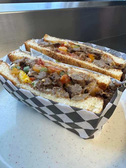 A sandwich filled with meat, vegetables, and cheese, served in a black and white checkered paper container.