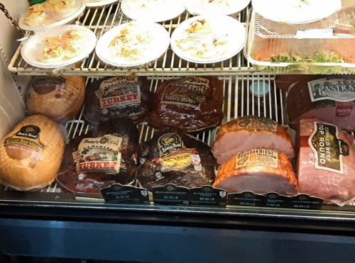 A display case filled with various packaged meats, including turkey, ham, and pastrami, with price tags visible.