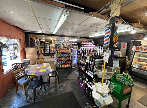 A cozy convenience store interior with shelves of snacks, drinks, and a small seating area. Brightly lit and inviting.