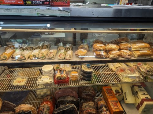 A display case filled with various packaged foods, including sandwiches, salads, and desserts.