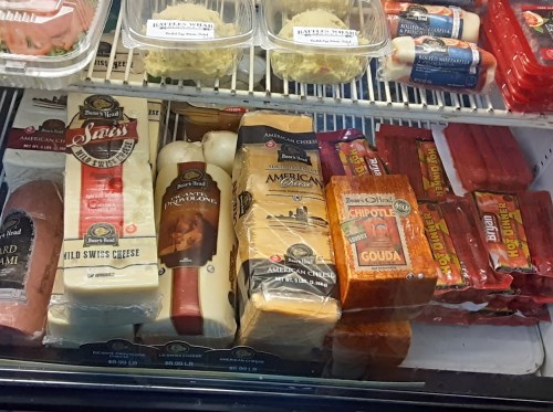 A display case filled with various types of cheese and deli meats, including sliced cheeses and packaged sausages.