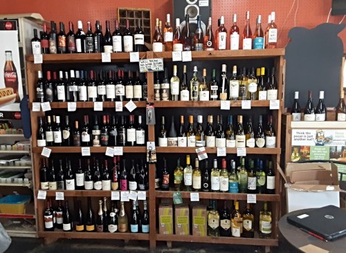 A wooden shelf displaying a variety of wine bottles, including reds, whites, and sparkling options, with price tags.